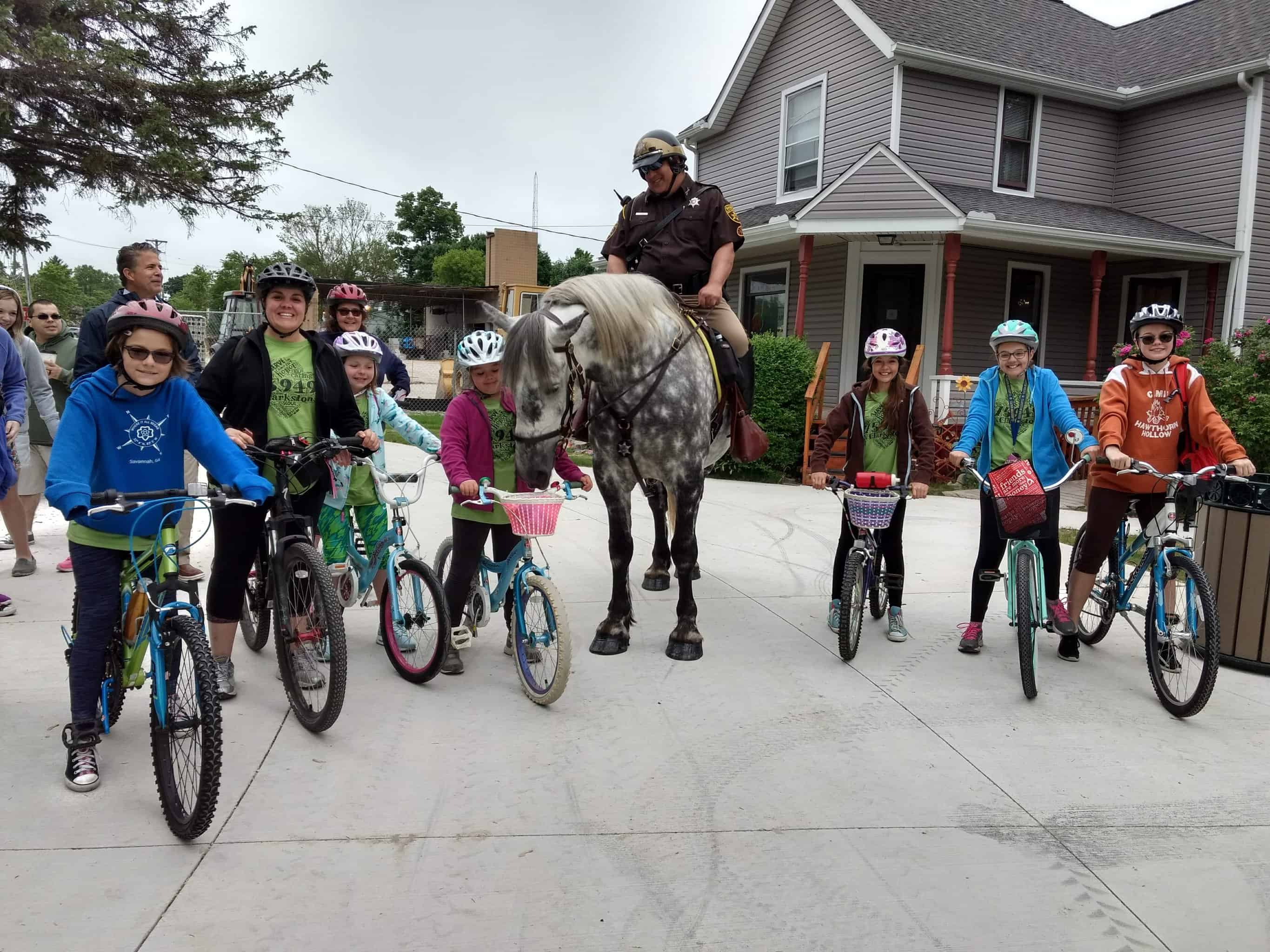 Cyclists get ready to enjoy the Paint Creek Trail by stopping to say hello to the mounted Oakland County Sheriff outside the Orion Art Center in Downtown Lake Orion